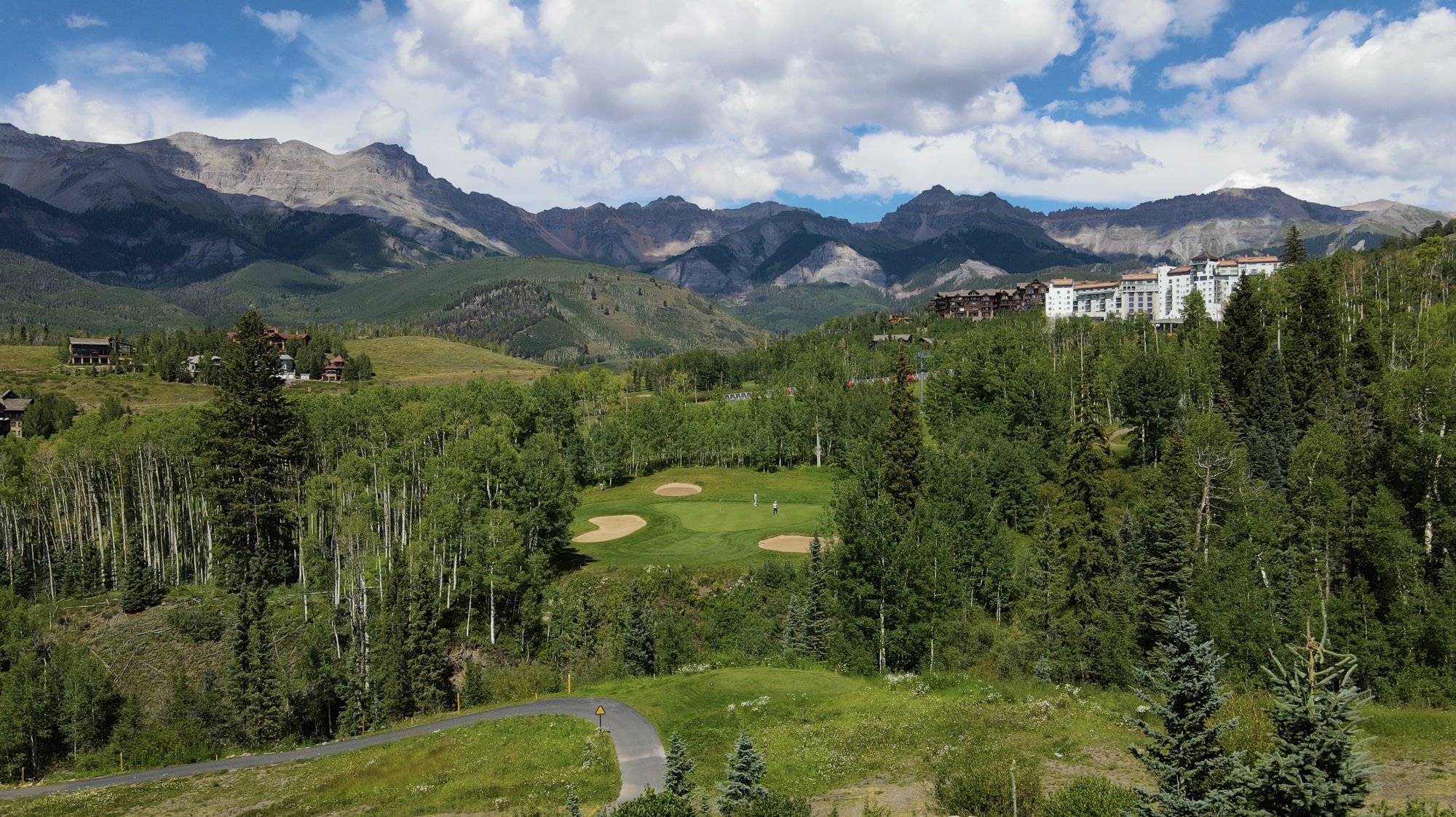 Aerial view of a mountain golf course in Telluride, Colorado, framed by aspen groves and the San Juan range with a luxury resort in the distance