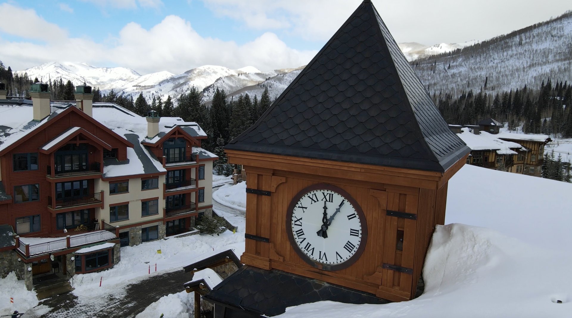 Close-up aerial of the signature clocktower at Solitude Mountain Resort in Utah's Wasatch Range — timber lodges in fresh snow with groomed runs rising behind