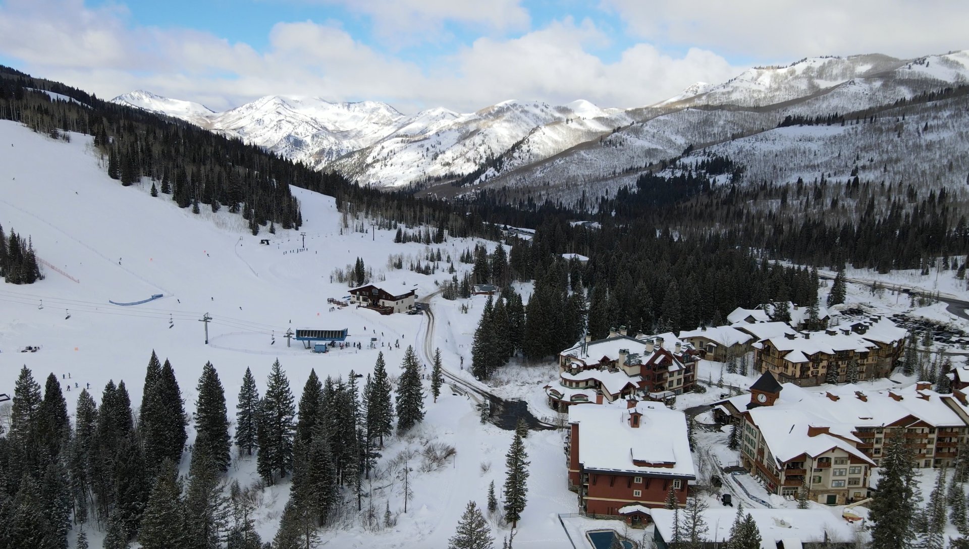 Aerial of a Colorado ski valley — snow-covered runs descending between spruce forest into a resort village at the foot of the mountain